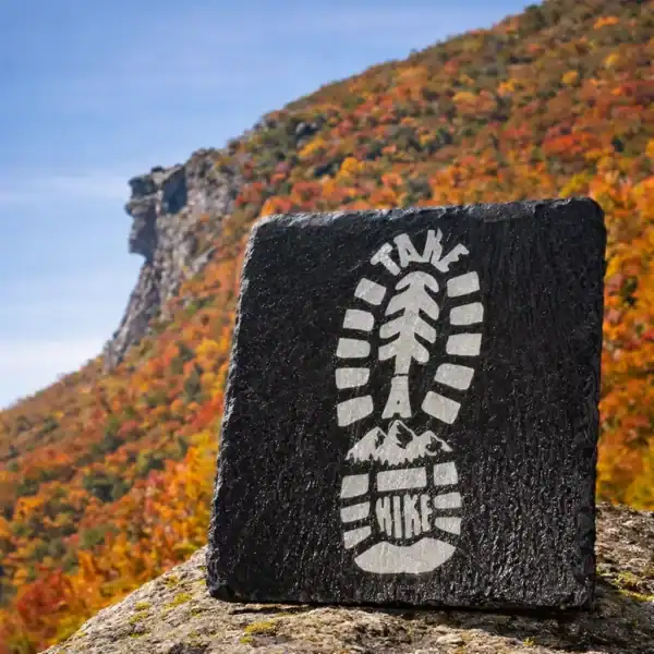 Laser engraved slate coaster with hiking boot design set against New Hampshire fall mountains