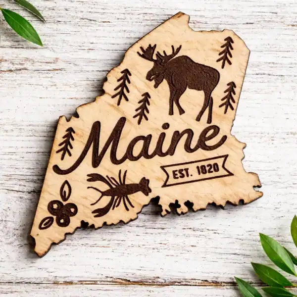 White Maine state–shaped wooden magnet with laser-engraved moose, pine trees, lobster, blueberries, and “Maine Est. 1820” design natrual wood