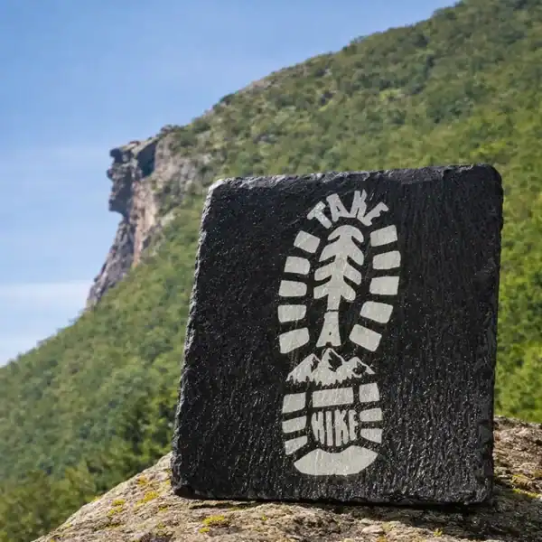 Black slate coaster engraved with hiking boot overlooking New Hampshire autumn foliage